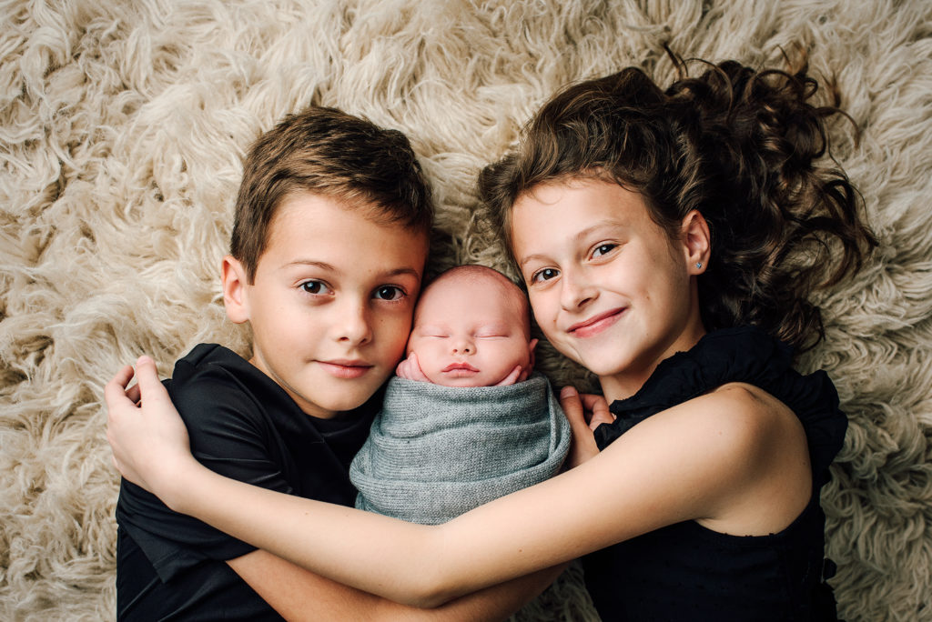 Portrait of older siblings with newborn brother on rug in Jacksonville, FL