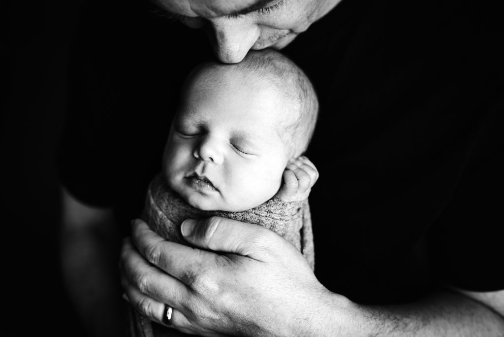Black and white portrait of dad kissing top of swaddled baby's head in Jacksonville, FL.