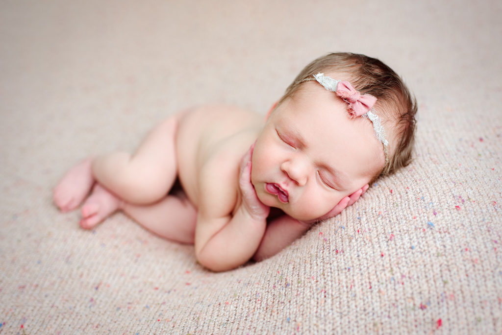 Side lying newborn girl with pink bow on speckled background in St. Johns, FL.