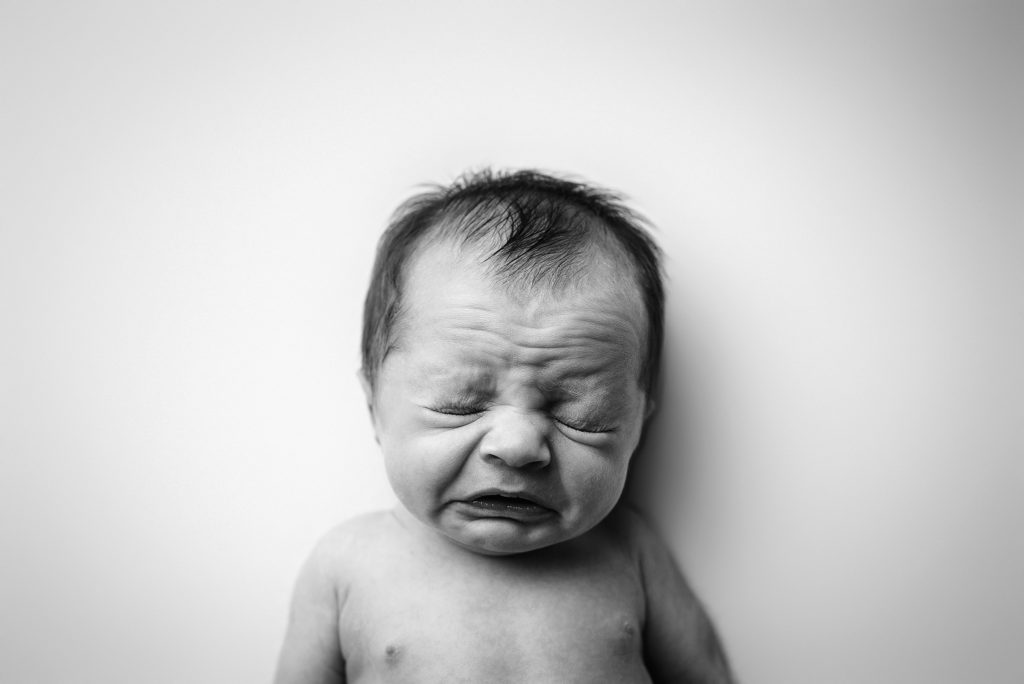 Black and white studio portrait of newborn boy sneezing in the San Marco area of Jacksonville, Florida.
