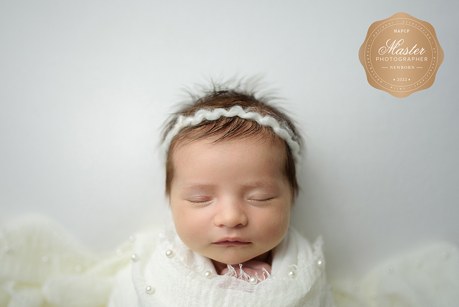 Studio newborn portrait of baby girl in white wrap and on white background in Ponte Vedra, FL.