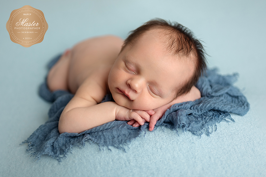Baby boy posed on blue backdrop with head on hands in Jacksonville, FL.