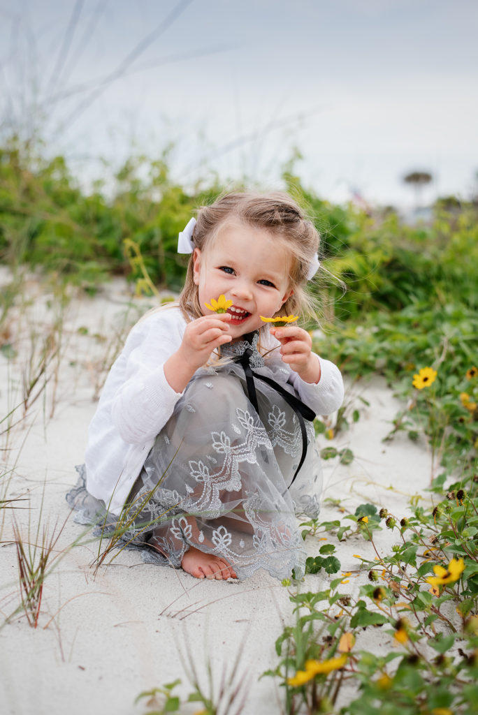 Girl in gray dress and white sweater picking flowers in Atlantic Beach, FL.