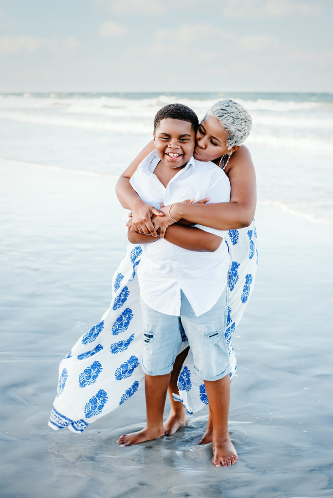Mom and older son in blue and white hugging on the beach in Atlantic Beach, FL.