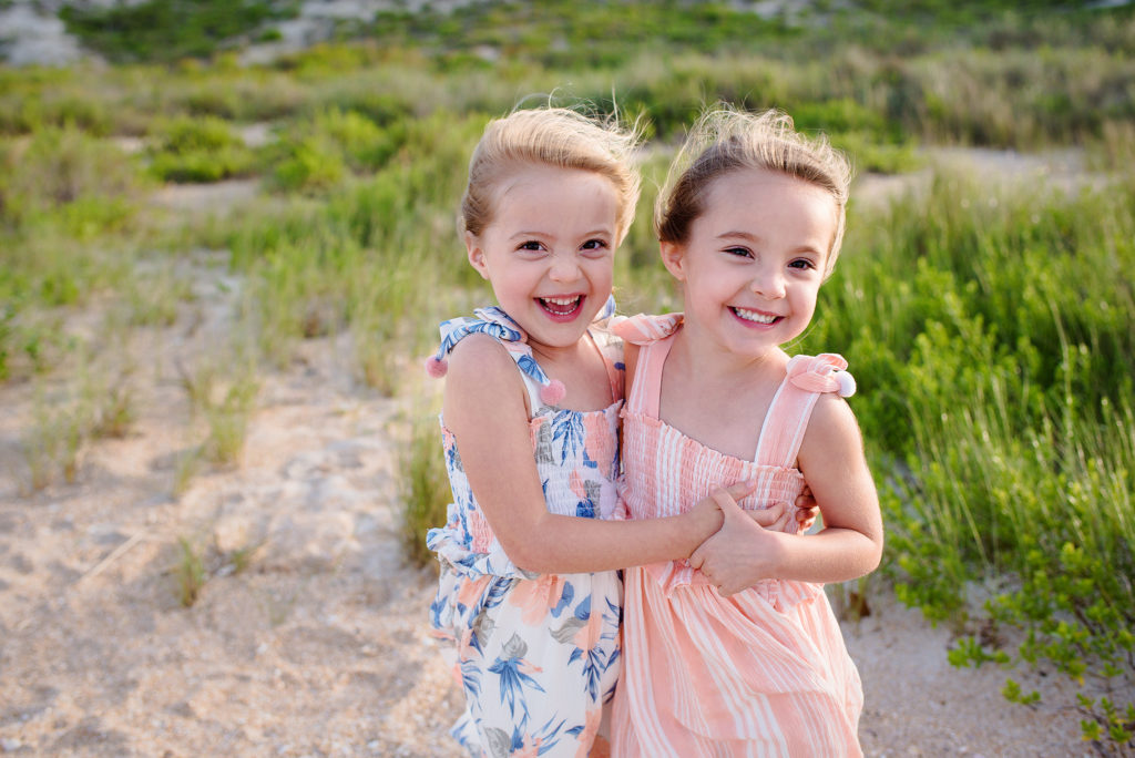Twin sisters wearing floral and striped dresses hugging and laughing at Guana Beach in Ponte Vedra, FL.