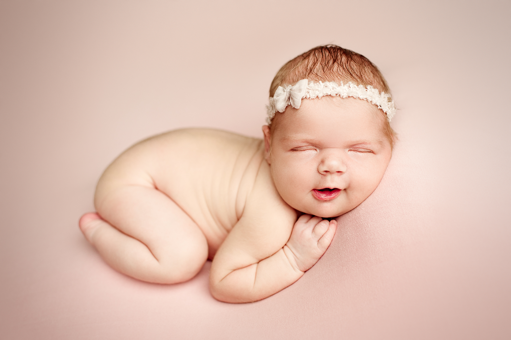 Studio newborn photo of smiling baby girl on pink background in Jacksonville, FL.