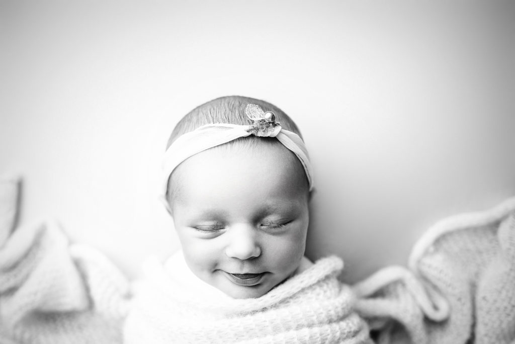 Black and white overhead image of smiling newborn girl with headband in Jacksonville, FL. 