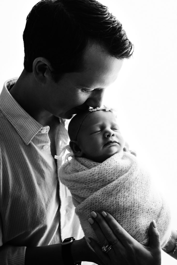 Black and white backlit portrait of dad kissing baby girl's head in Atlantic Beach, FL.