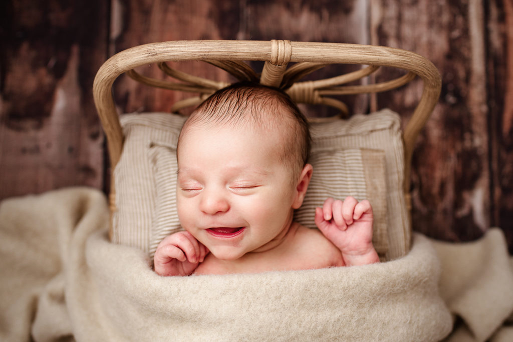 Smiling newborn boy lying in neutral colored baby bed in Jacksonville, FL. 