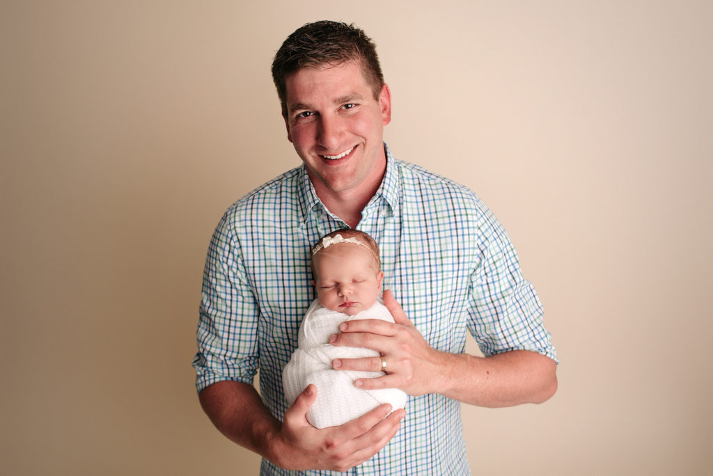 Dad in plaid shirt holding swaddled baby girl for studio newborn session in St. Johns, FL.