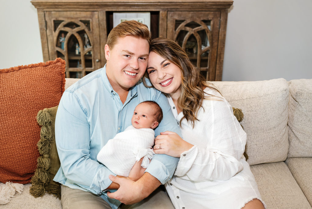 Mom and dad holding swaddled baby boy on couch for lifestyle newborn session in St. Augustine, Florida.